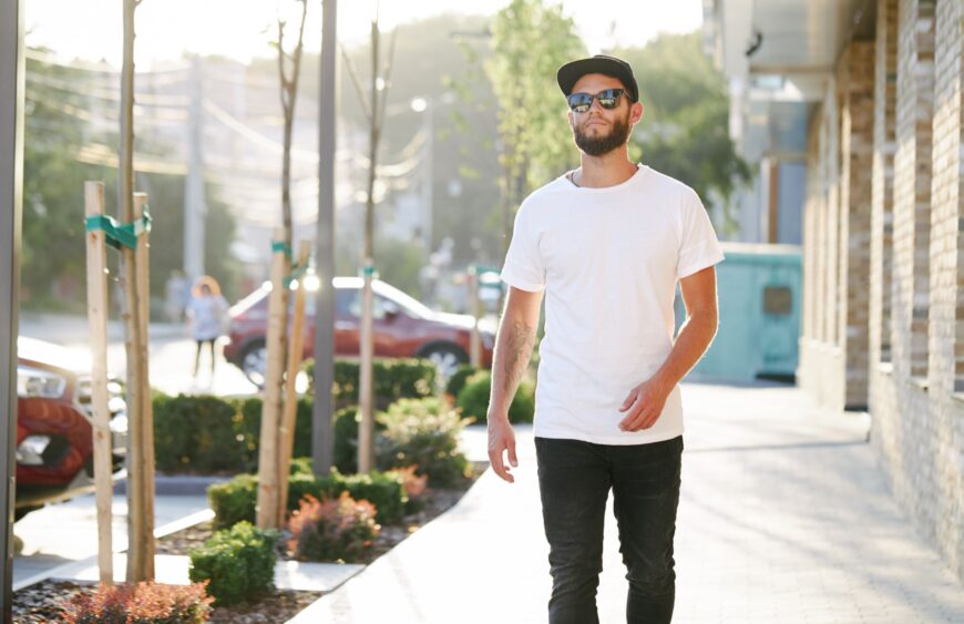 Hipster handsome male model with beard wearing white blank t-shirt and a baseball cap with space for your logo or design in casual urban style